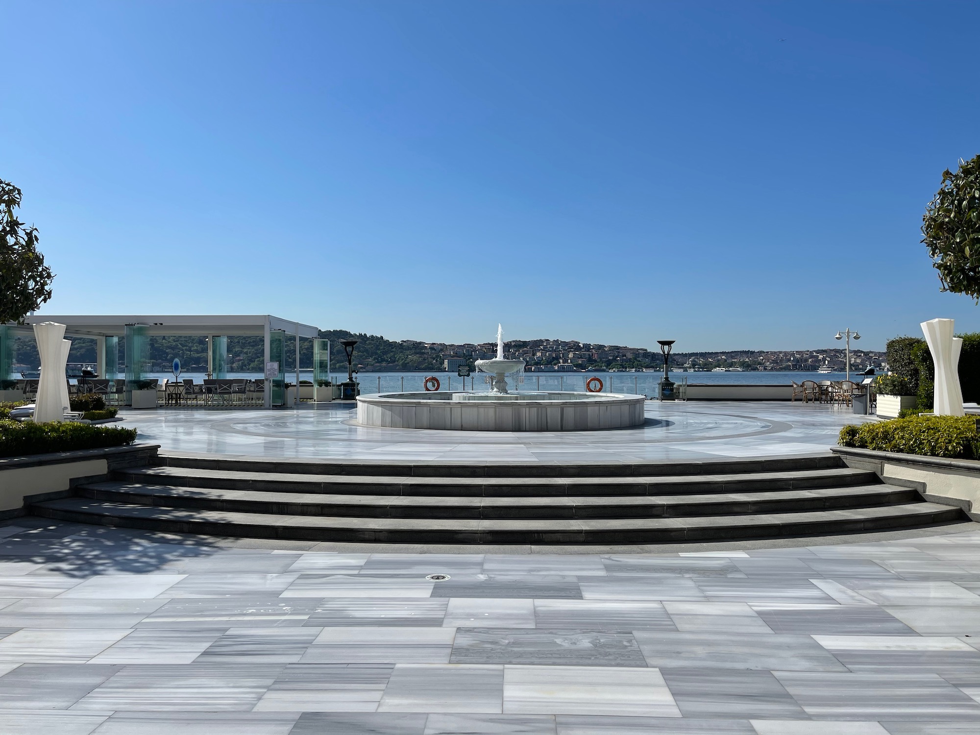 a circular fountain with steps and a water body in the background