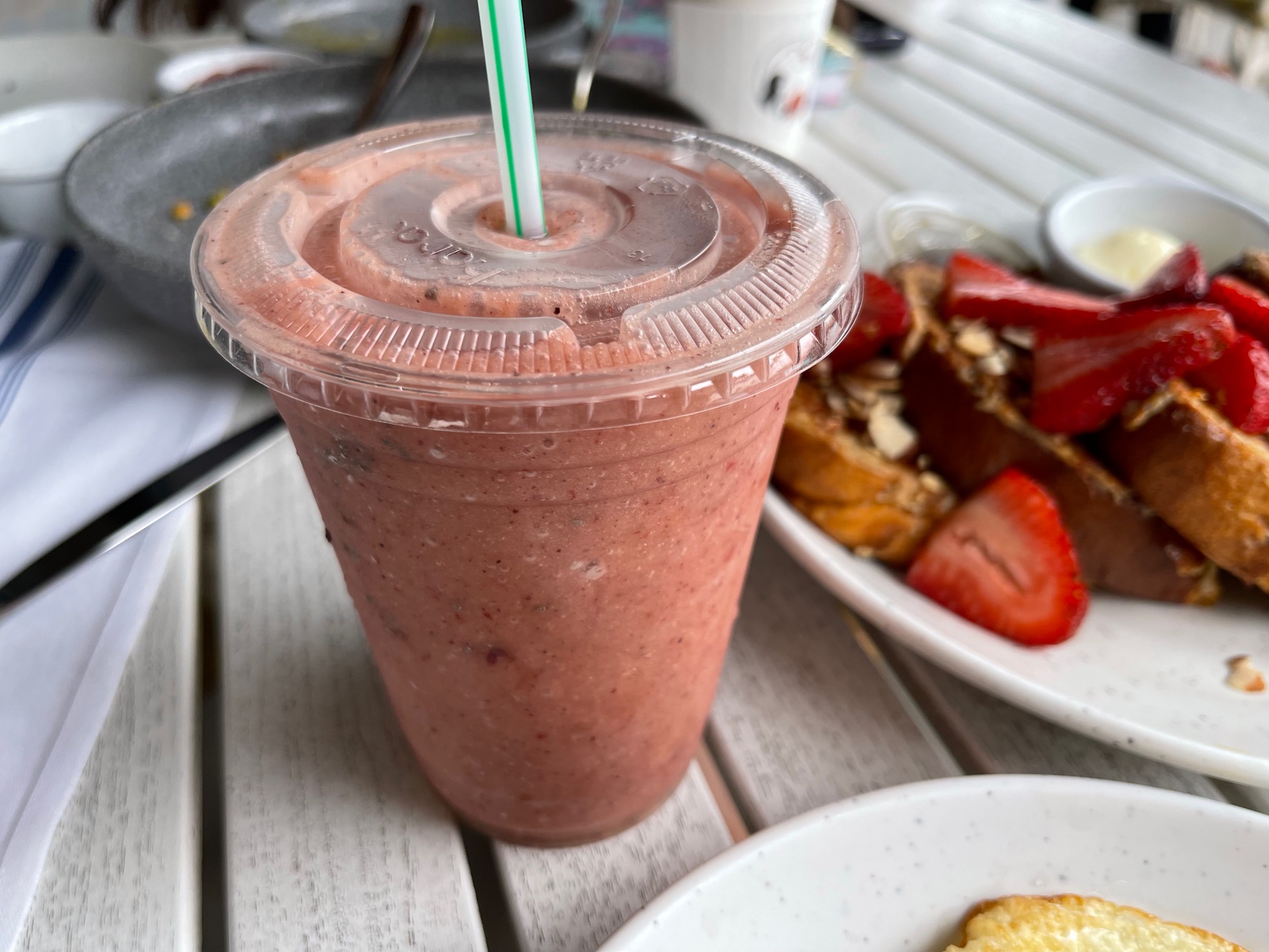 a pink smoothie in a plastic cup with straw and a plate of food