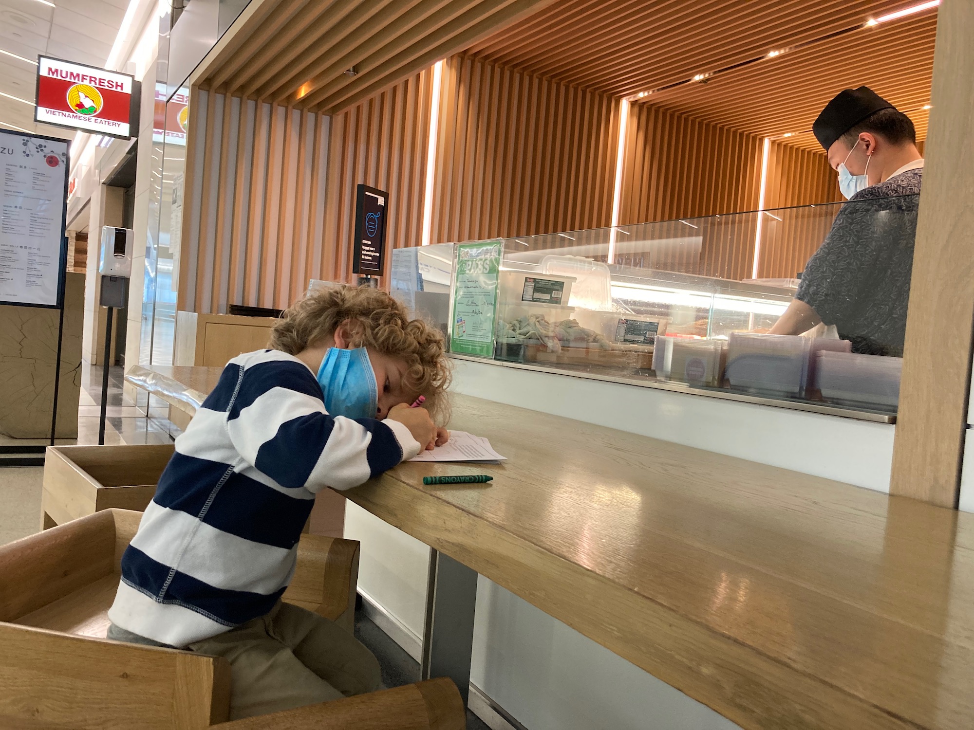 a boy with face mask sitting at a table with a child in a restaurant