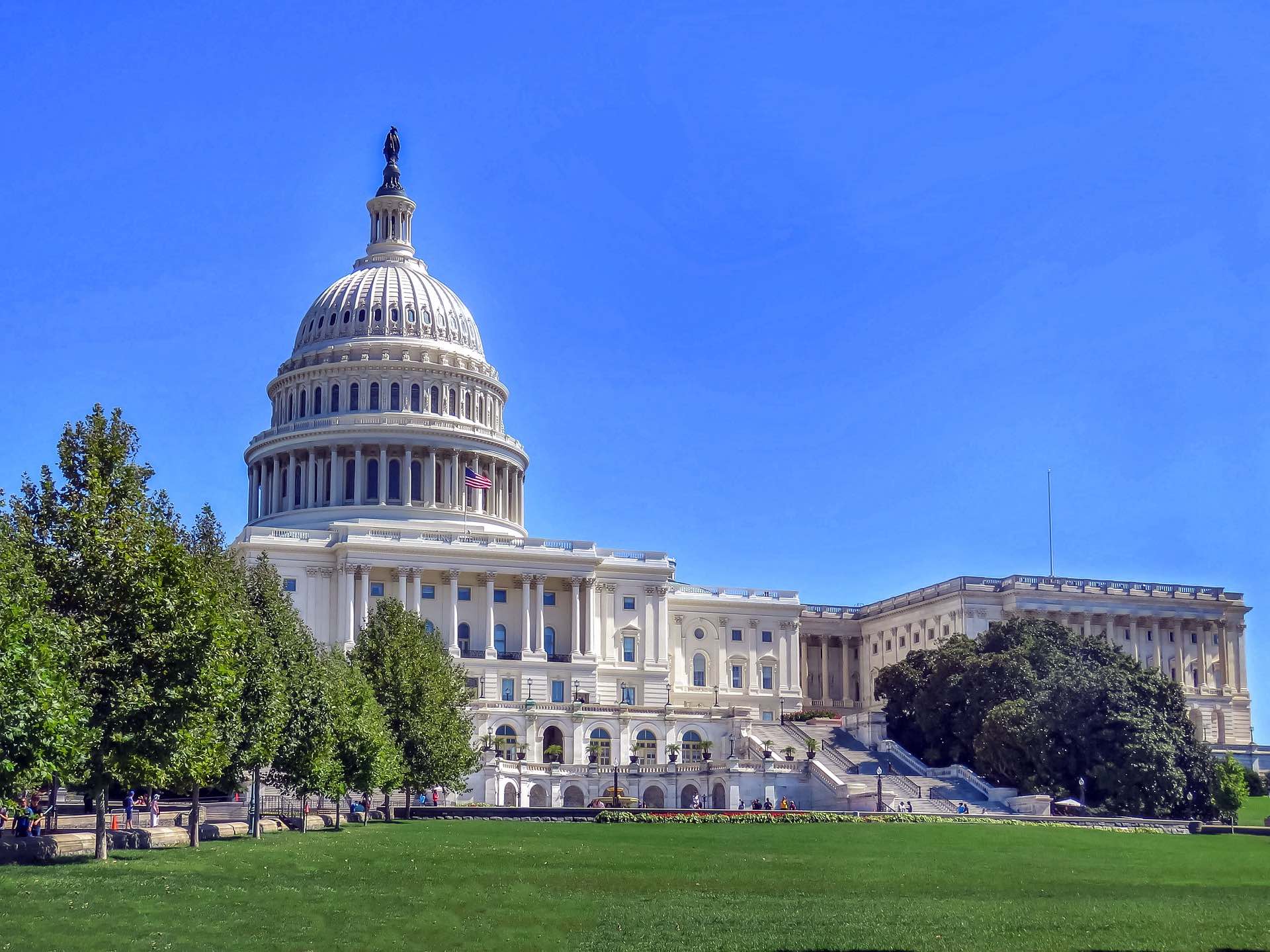 a large white building with a dome and a lawn with United States Capitol in the background