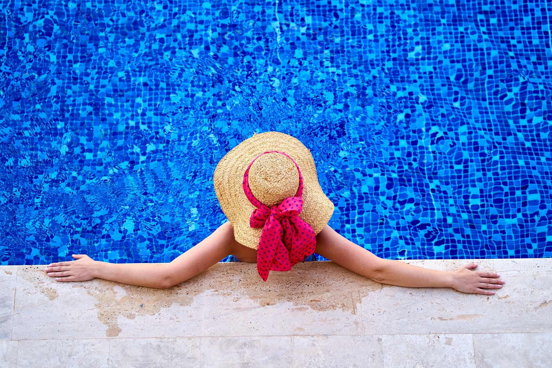 a woman in a hat leaning on a pool edge