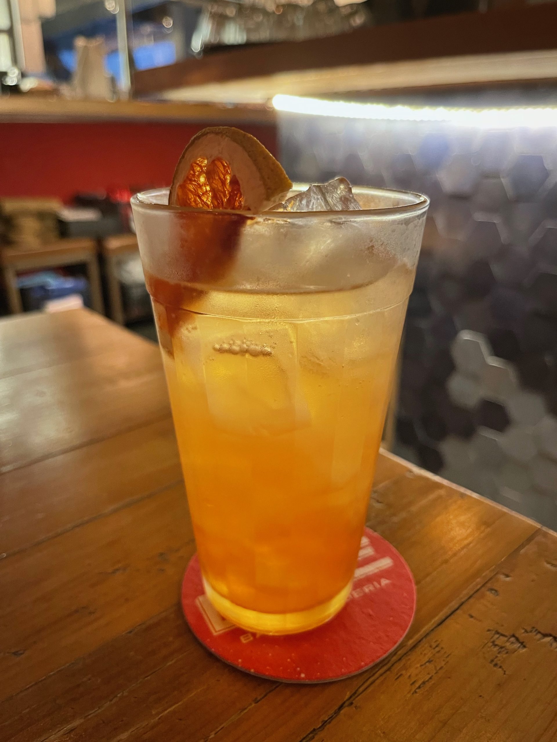 a glass of orange liquid with ice and a slice of orange on a coaster