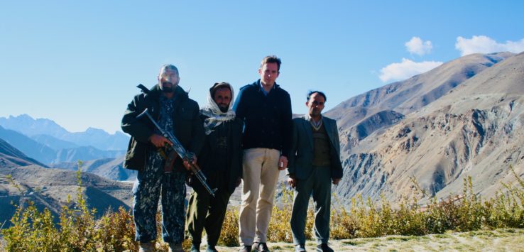 a group of men standing on a hill with mountains in the background