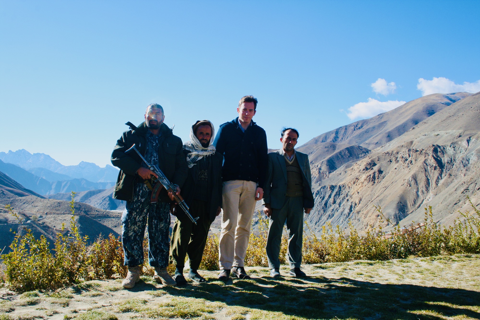 a group of men standing on a hill with mountains in the background