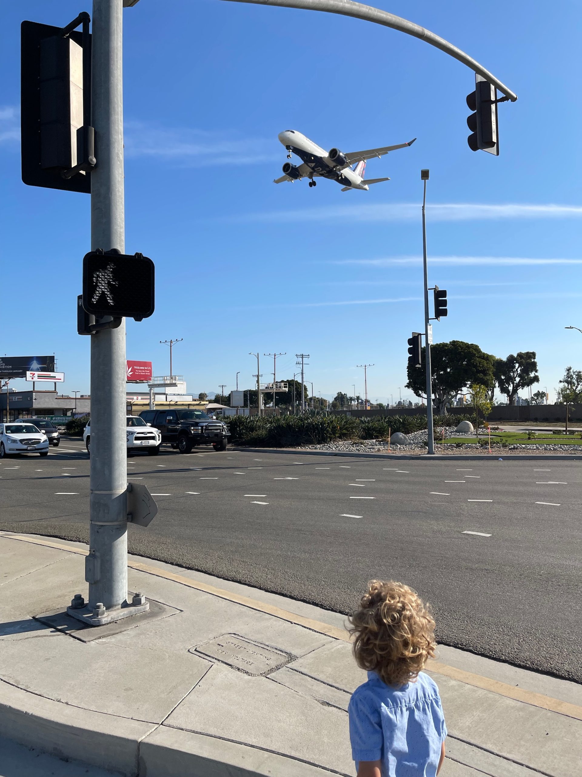 a child looking at an airplane flying over a street