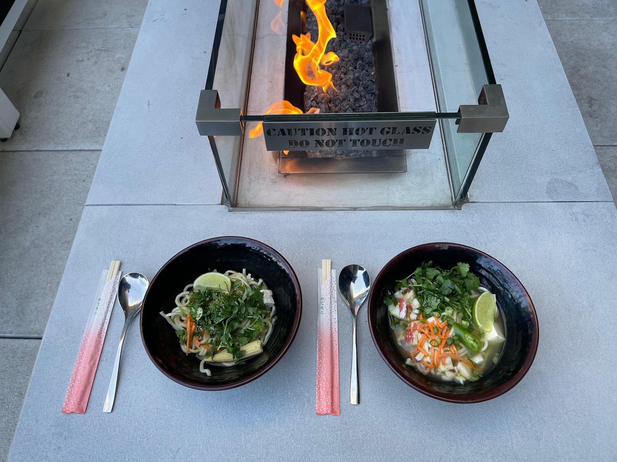 bowls of soup and noodles on a table next to a fire