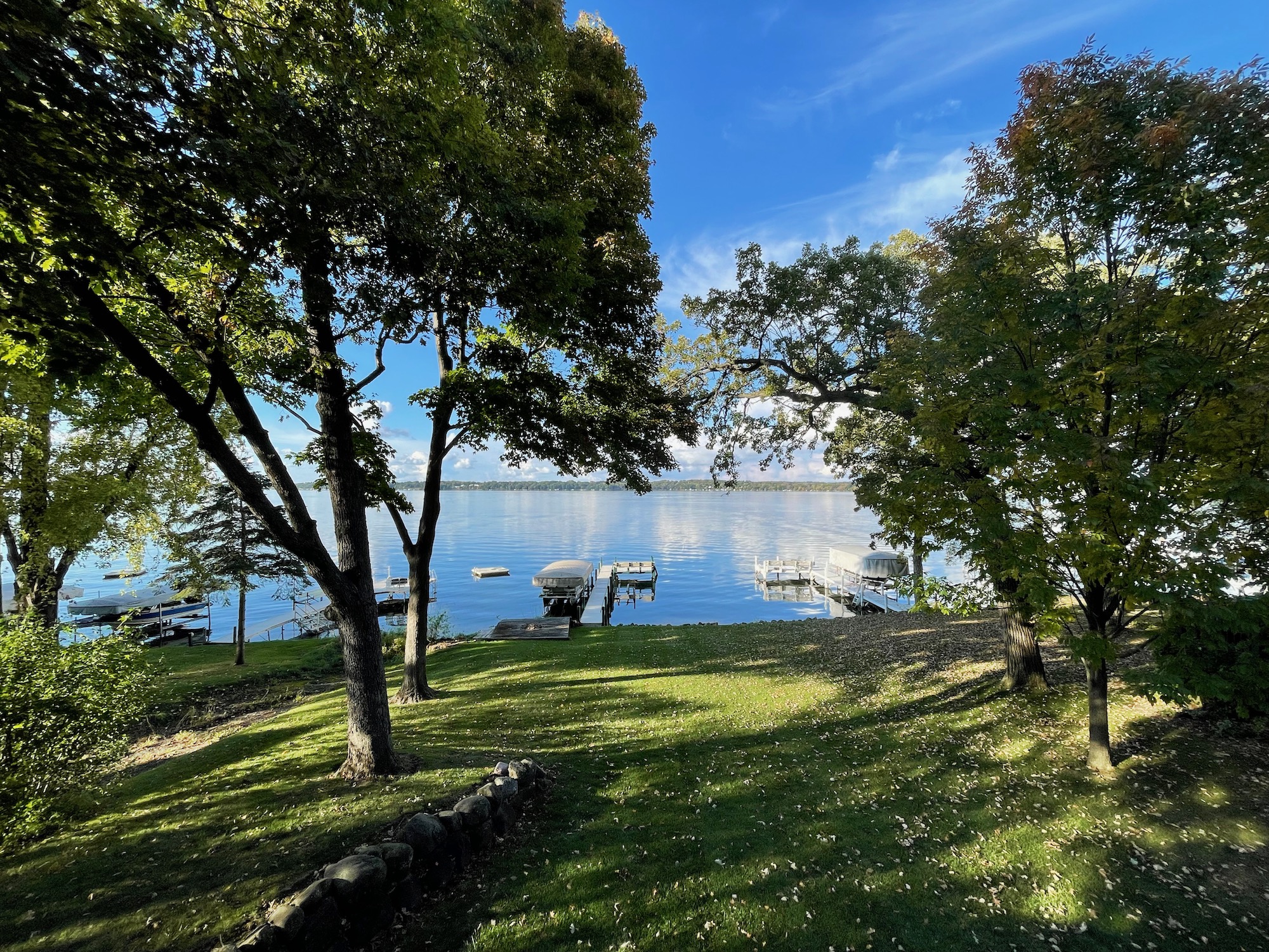 a grassy hill with trees and a dock on the water