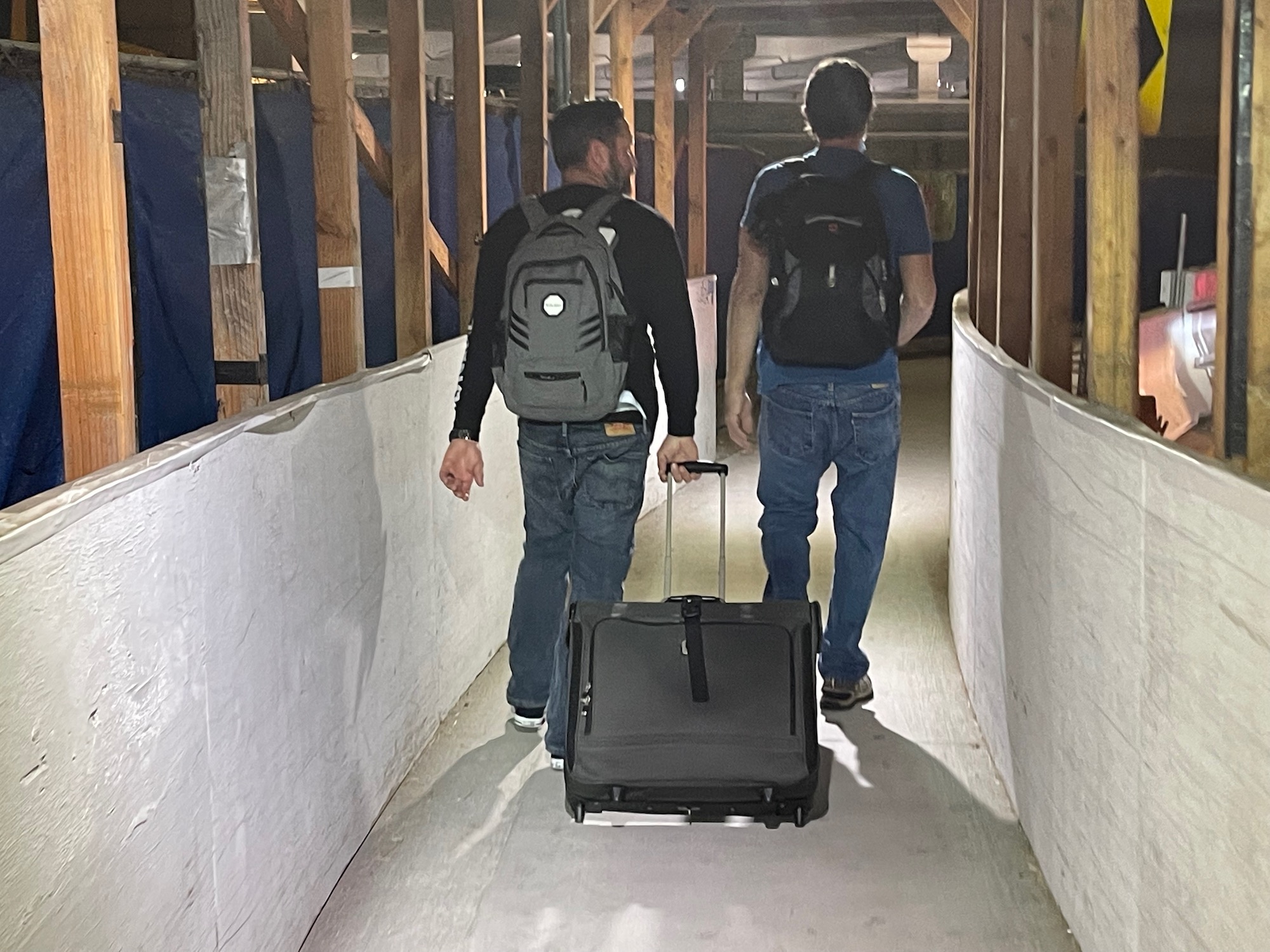 two men with backpacks walking down a tunnel with luggage