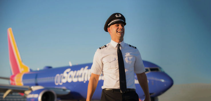 a man in uniform and hat standing in front of a plane