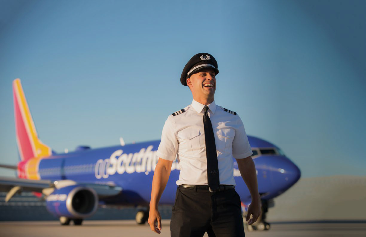 a man in uniform and hat standing in front of a plane