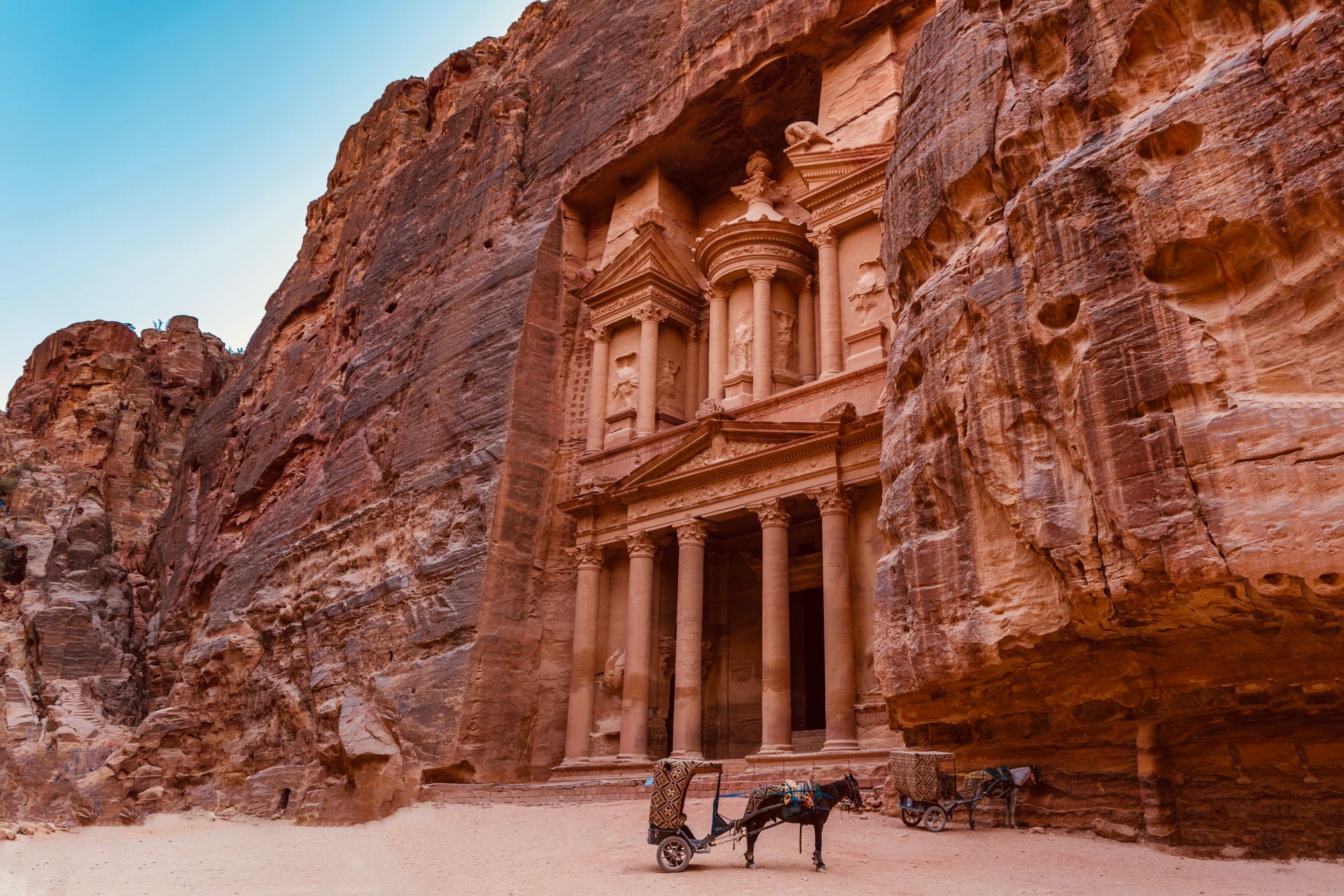 a horse pulling a cart in front of a rock formation with Petra in the background