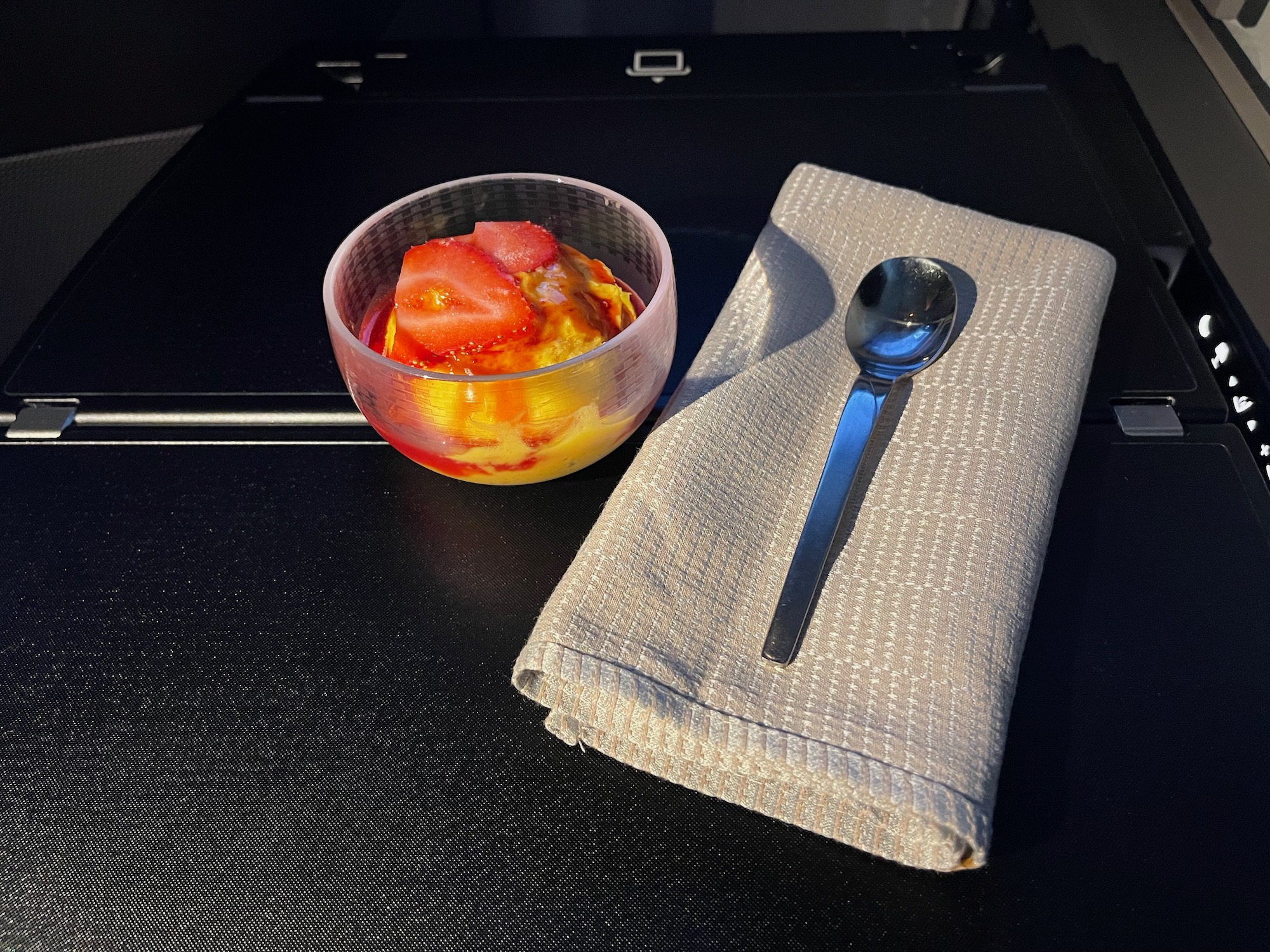 a bowl of ice cream with strawberries and a spoon on a napkin