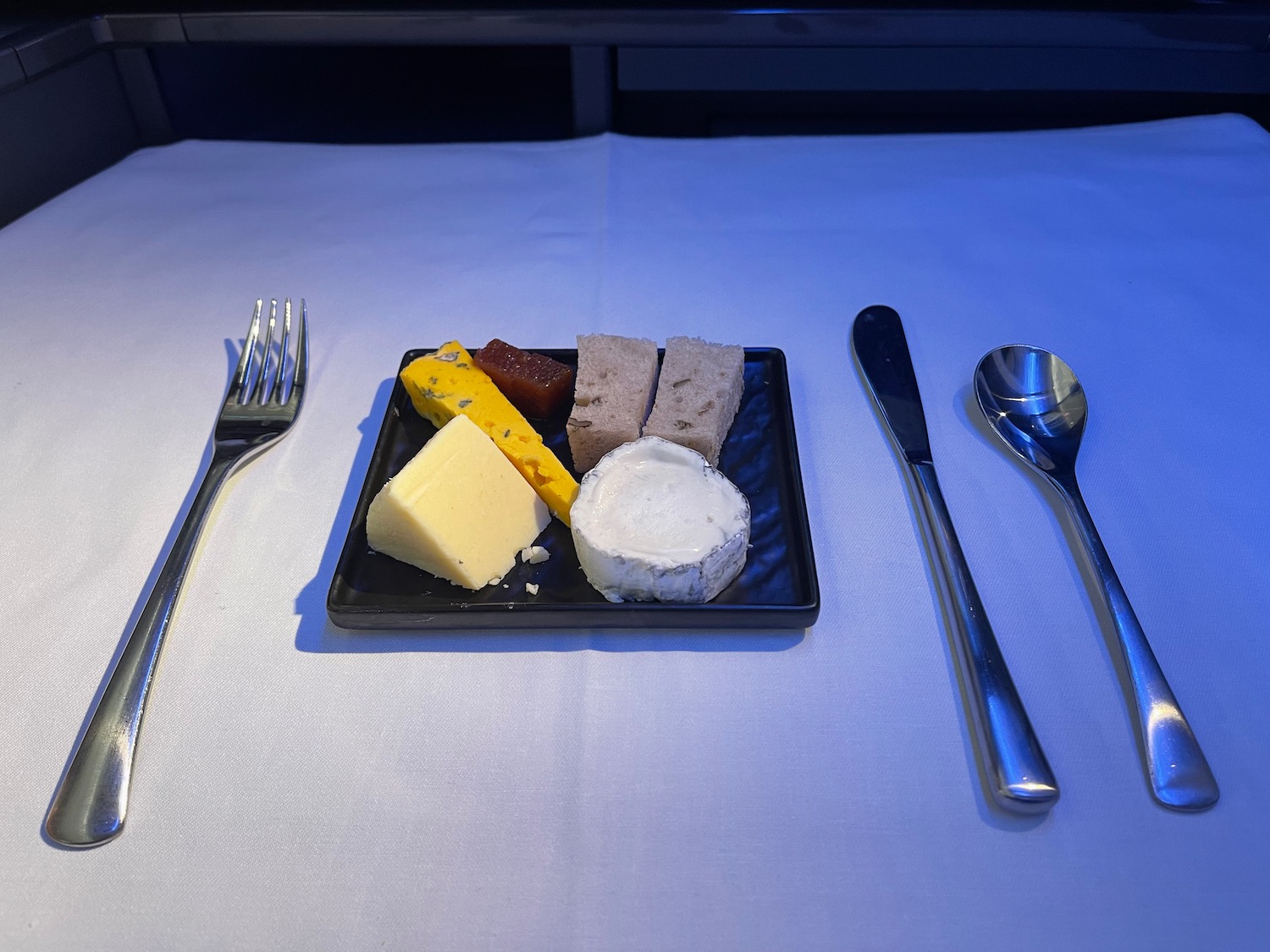 a plate of cheese and bread on a table with a spoon and fork