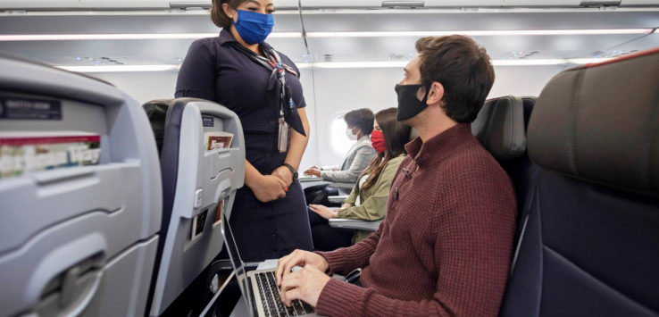 a man and woman wearing face masks and using a laptop on an airplane