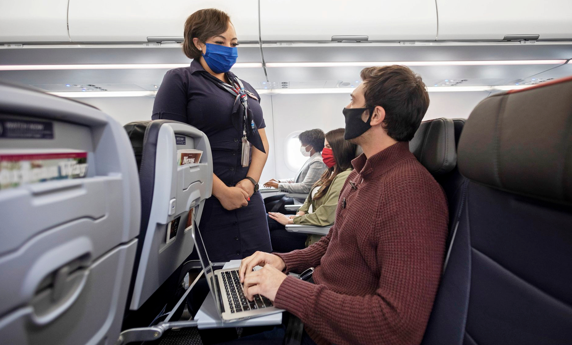 a man and woman wearing face masks and using a laptop on an airplane