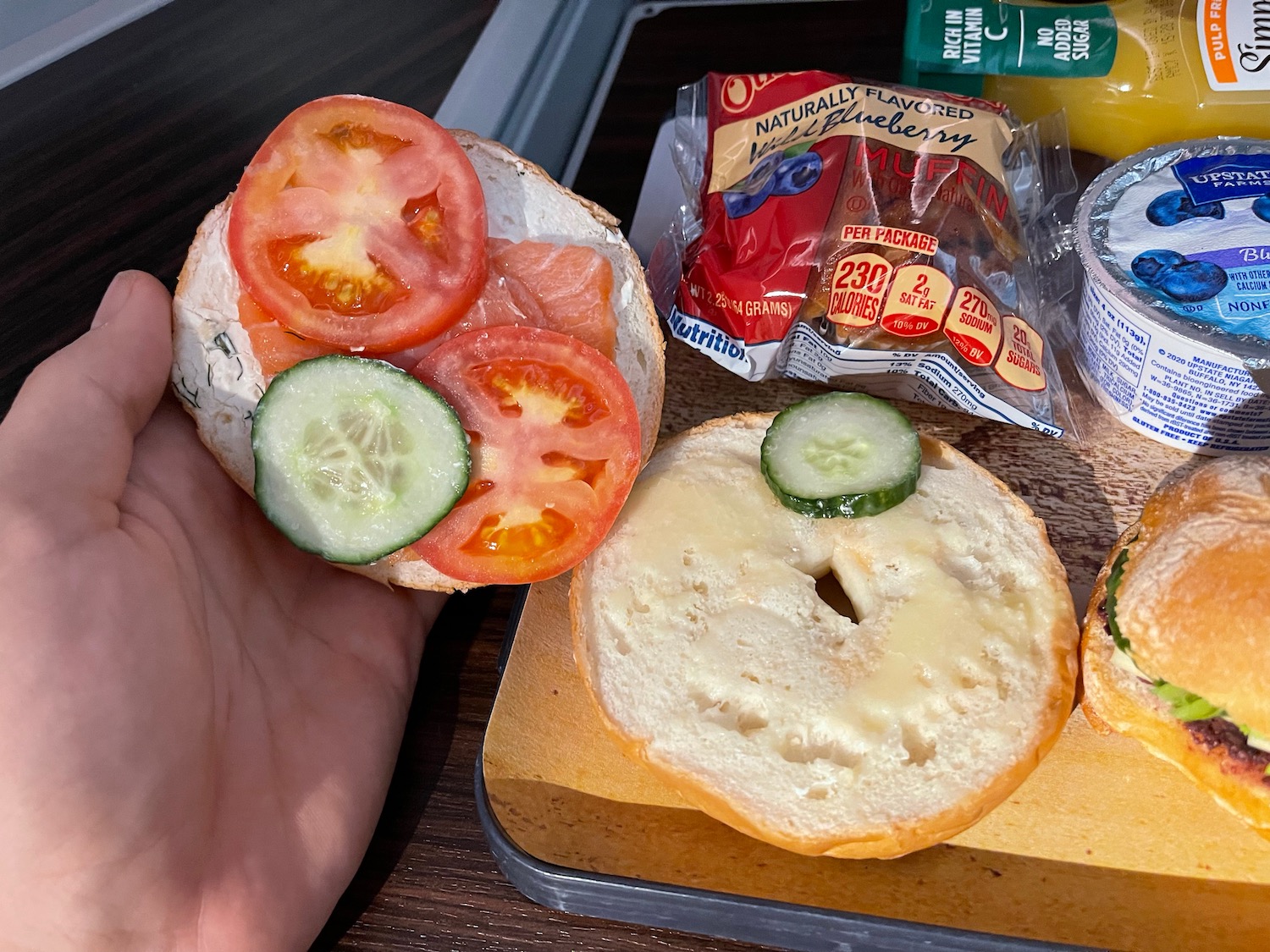 a hand holding a bagel with tomatoes cucumbers and cheese