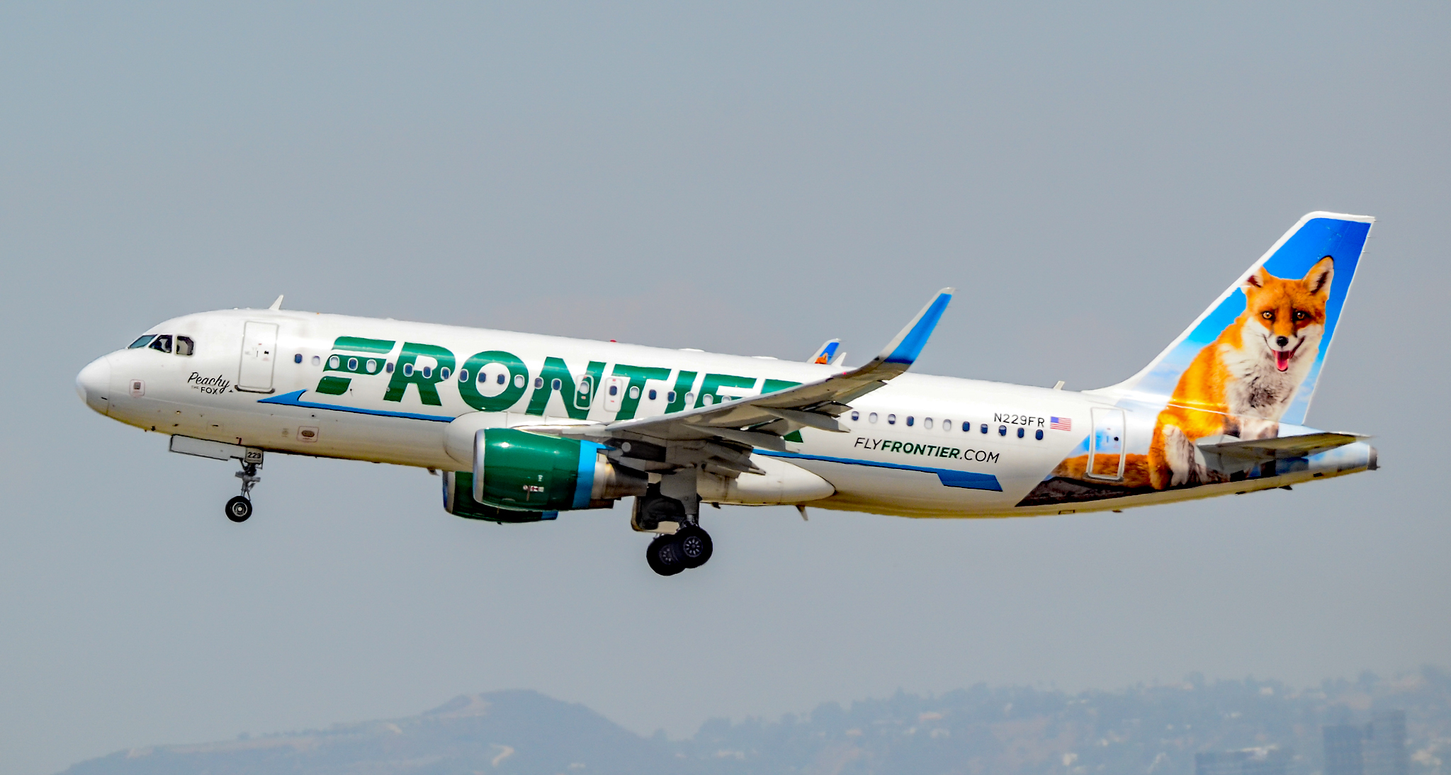 a white airplane with green and blue text flying in the sky