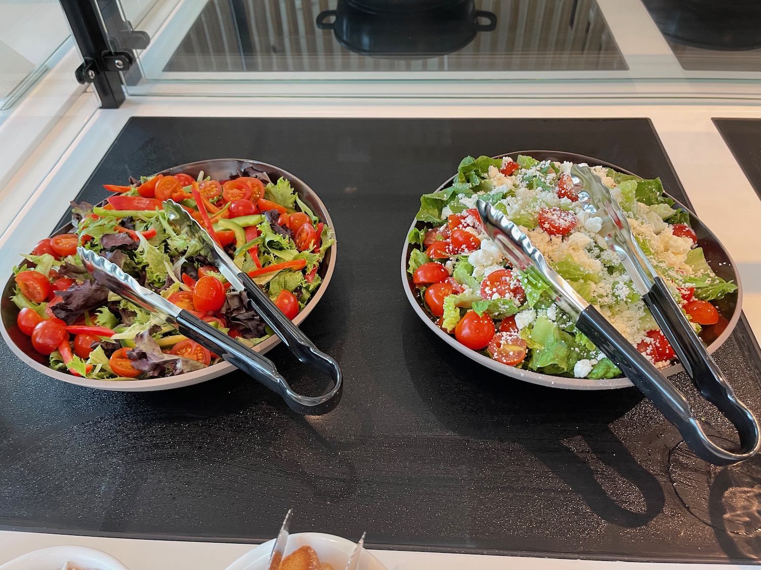 two bowls of salad with tongs