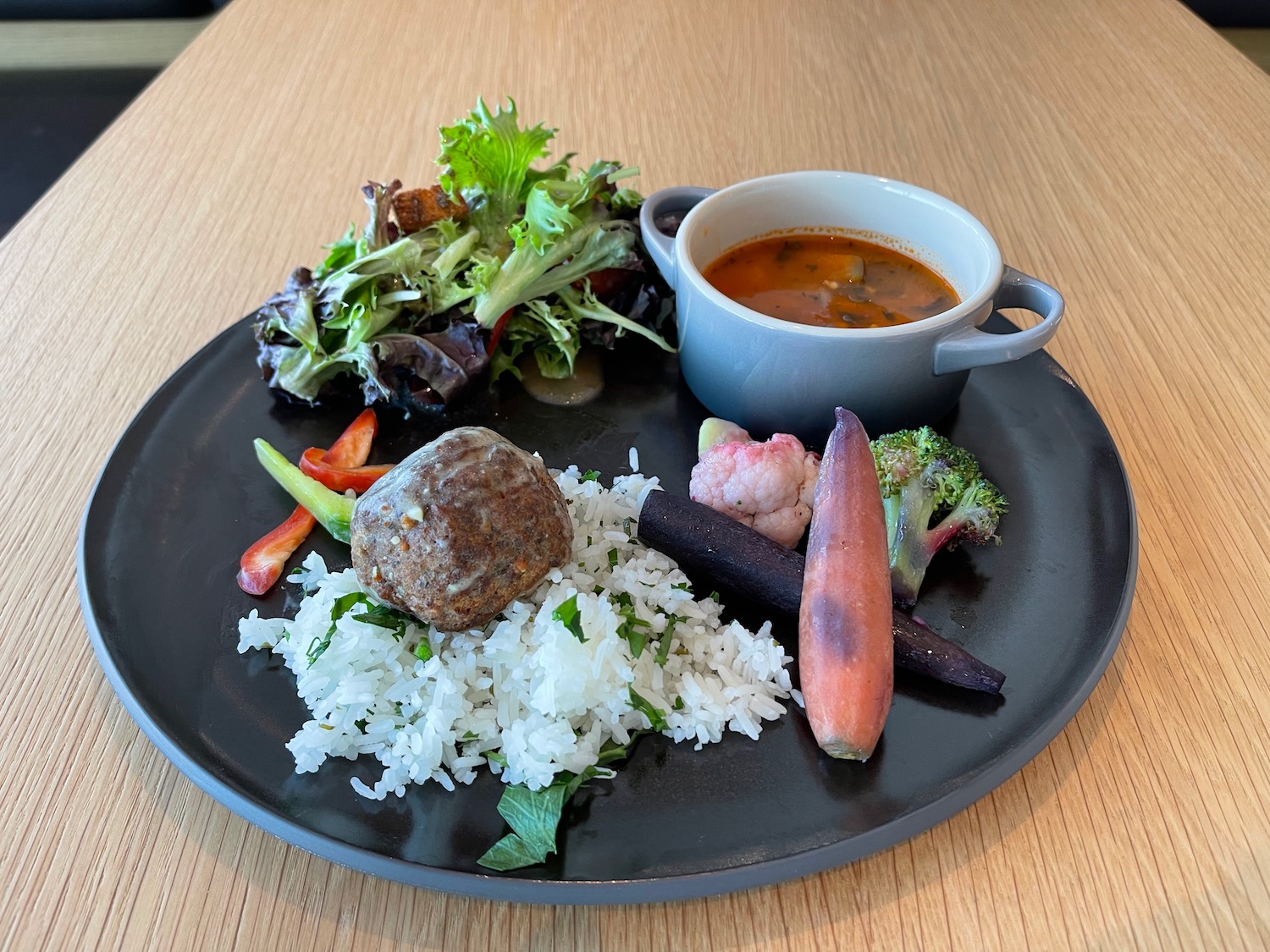 a plate of food with a bowl of soup and a meatball on it