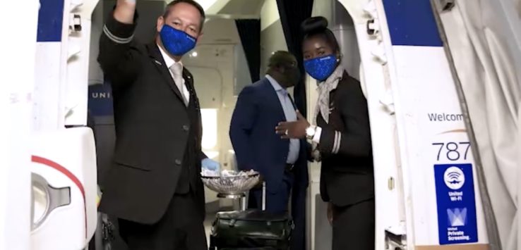 a man and woman wearing face masks and standing in an airplane