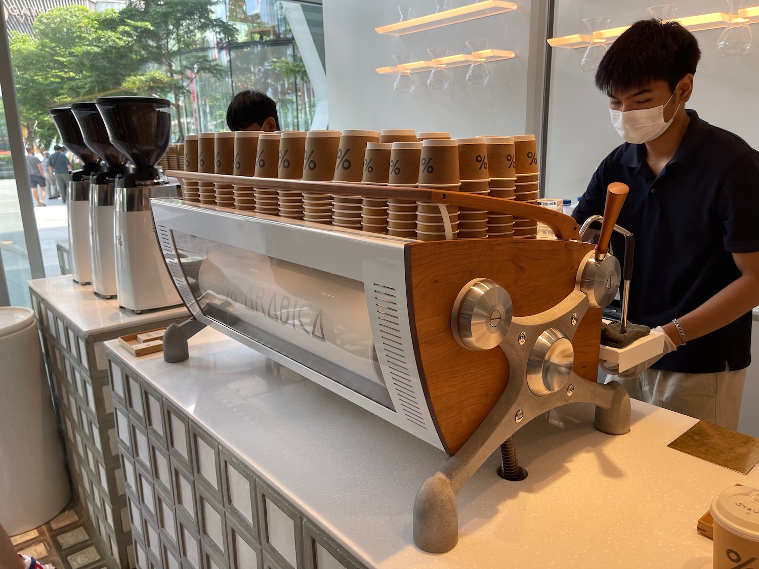 a person wearing a mask behind a machine with many cups