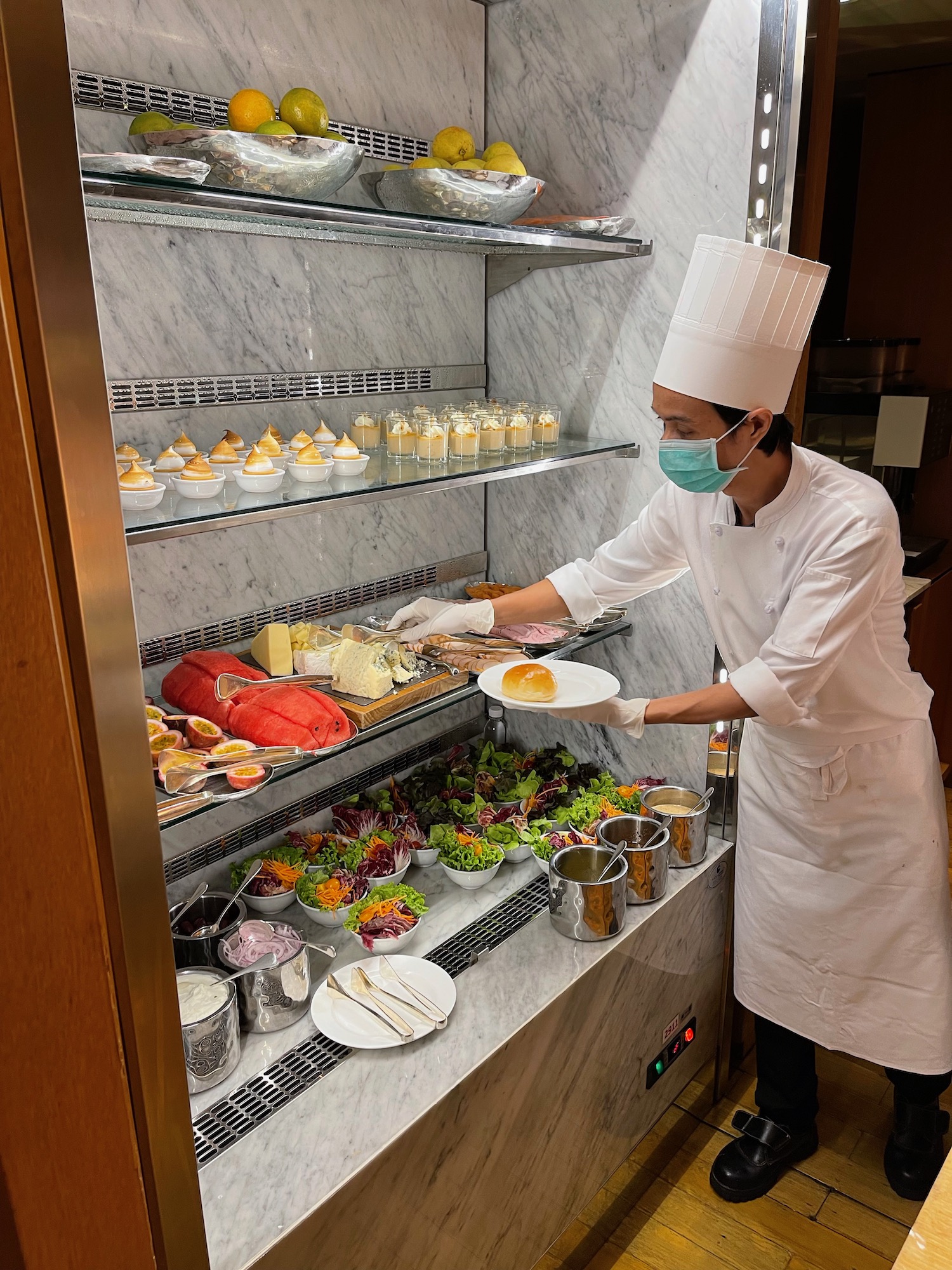 a chef wearing a mask and gloves holding food in a display case