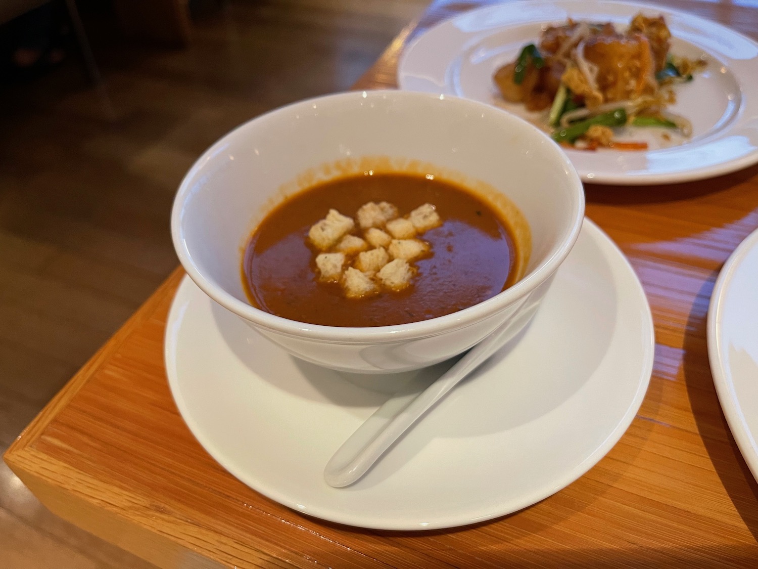 a bowl of soup with croutons on top of a plate of food
