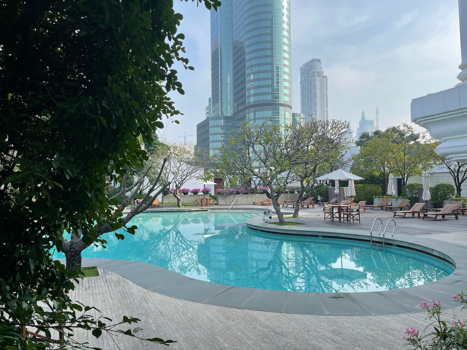 a pool with chairs and trees in front of a building