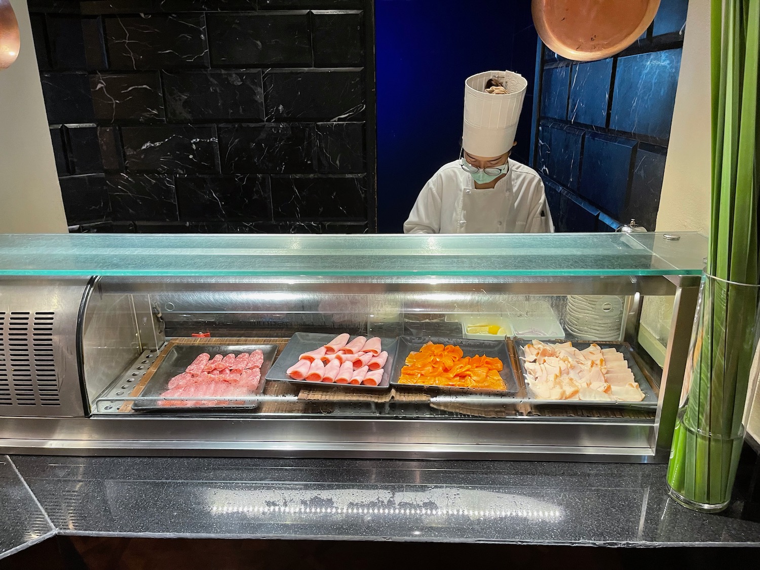 a chef in a white uniform behind a counter with trays of meat