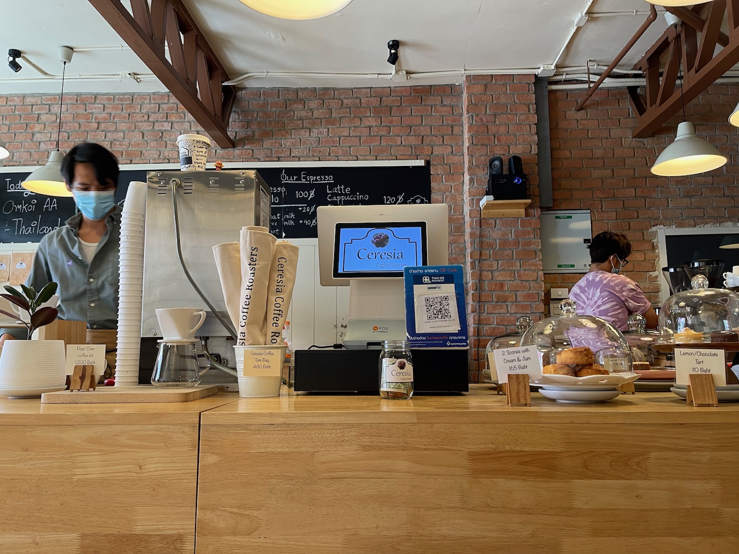 a woman wearing a mask behind a counter in a coffee shop