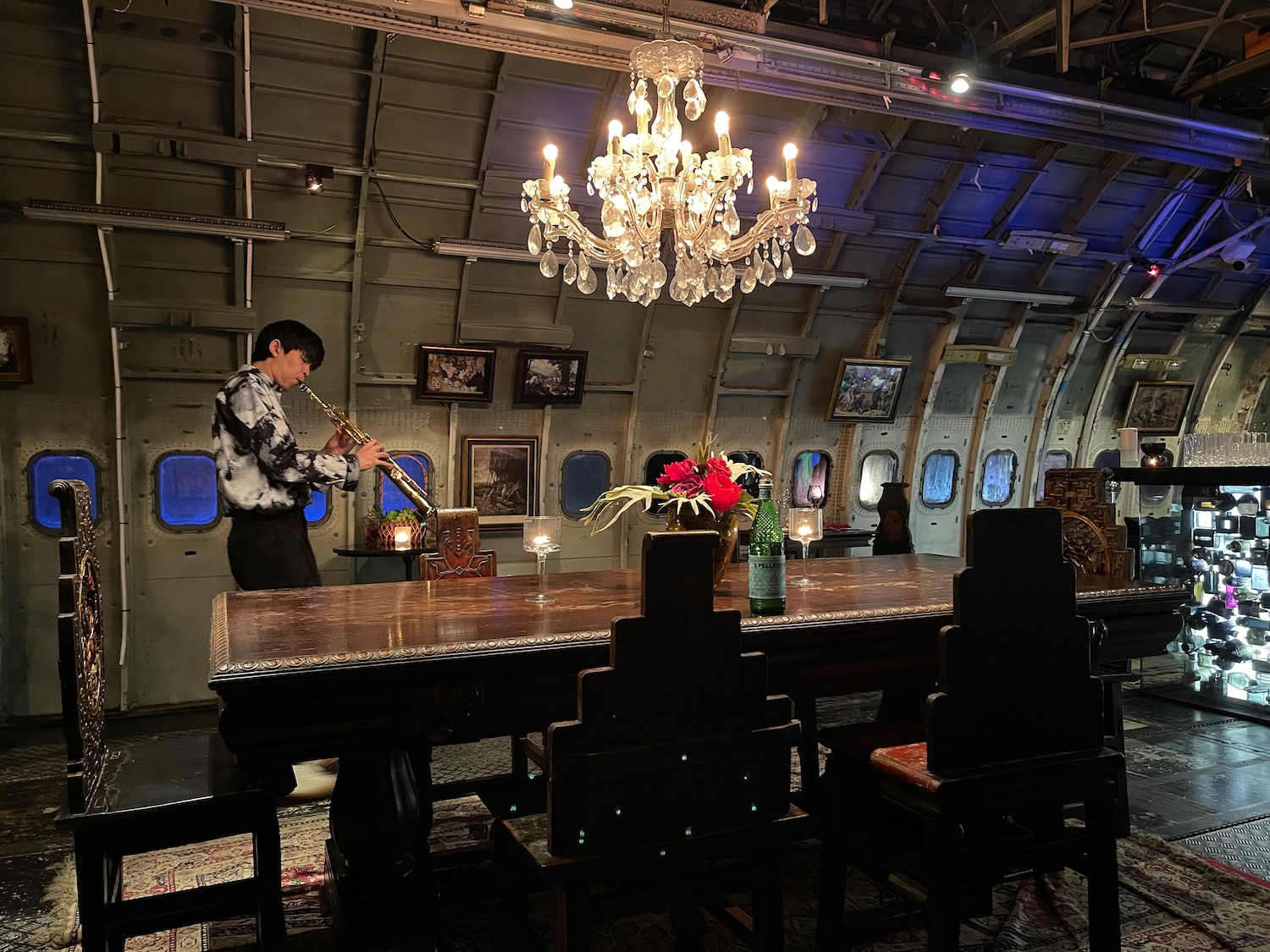 a man playing a flute in a room with chairs and a chandelier