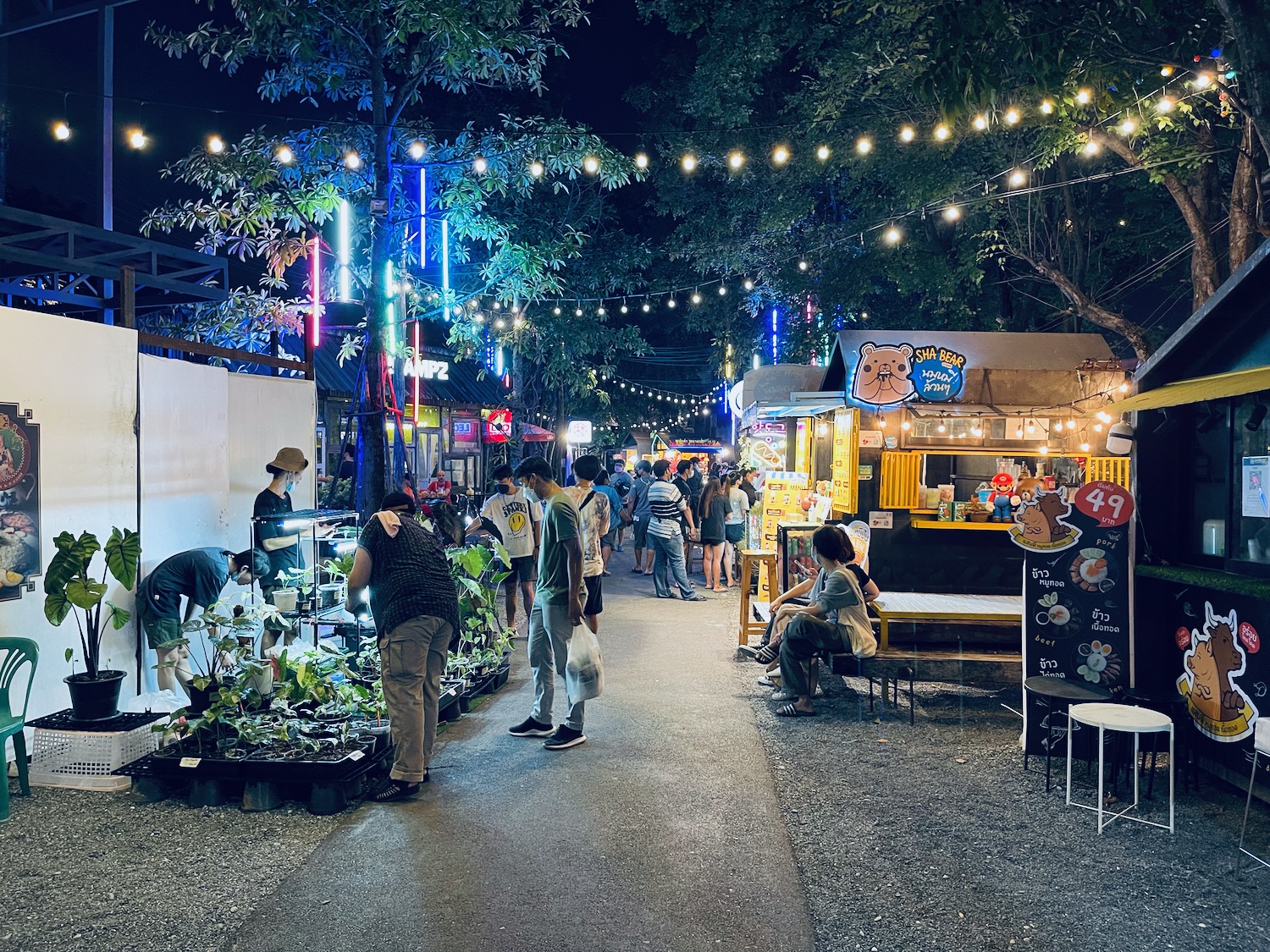 people walking on a sidewalk with food stalls and lights
