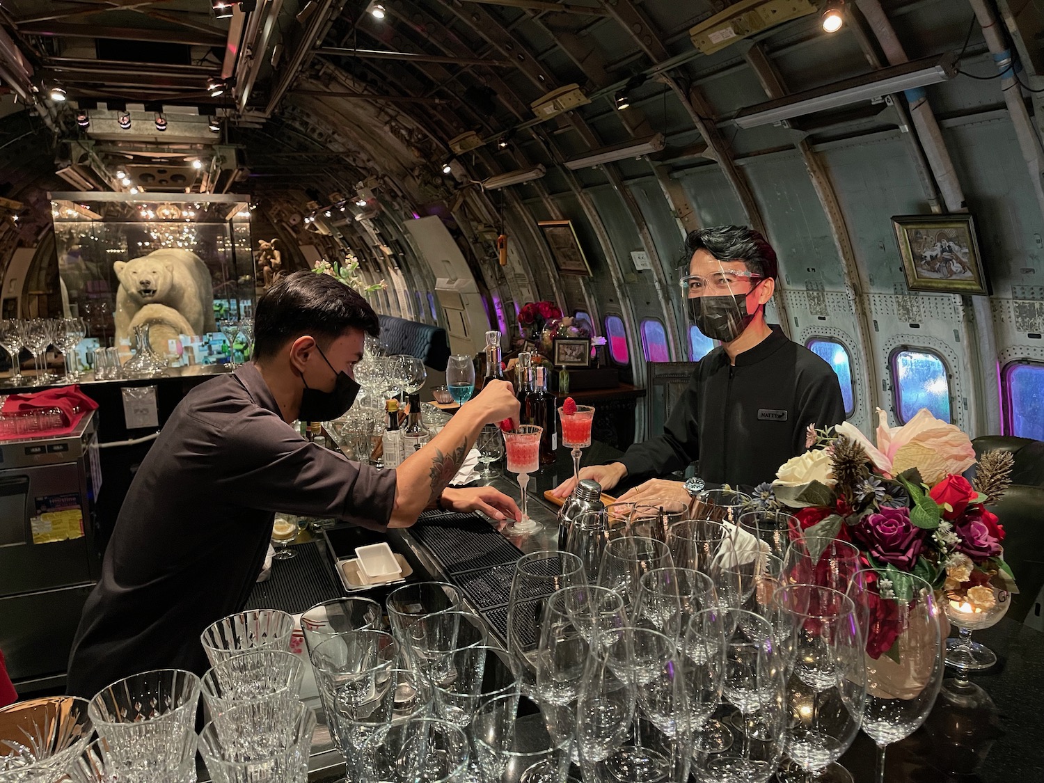 a man wearing a face mask behind a bar with glasses and drinks