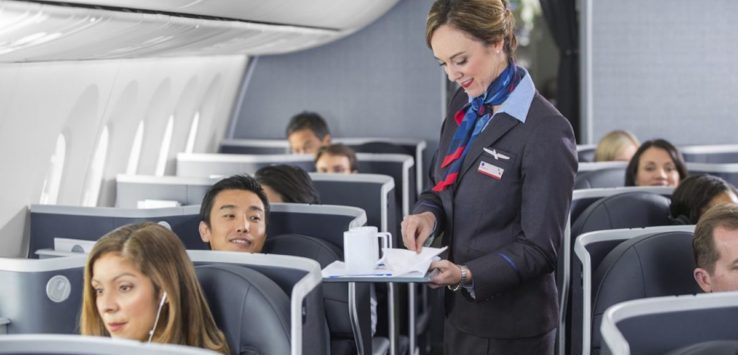 a woman holding a tray with people in the back of a plane