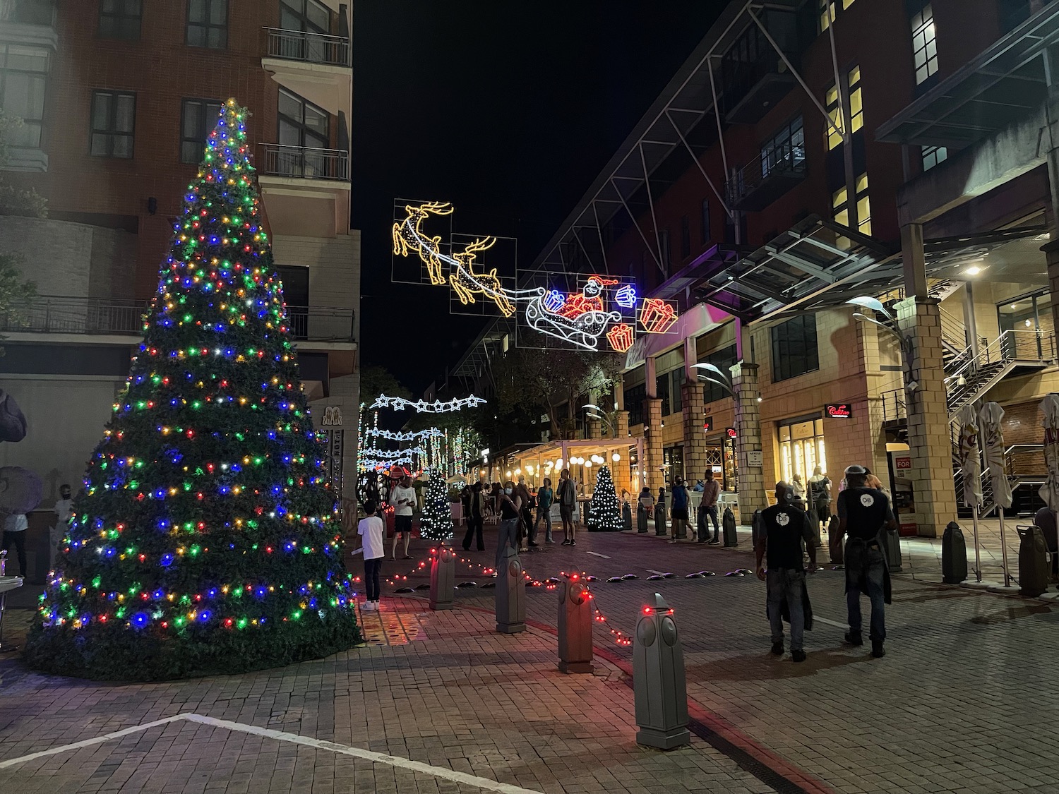 a group of people walking on a street with a christmas tree