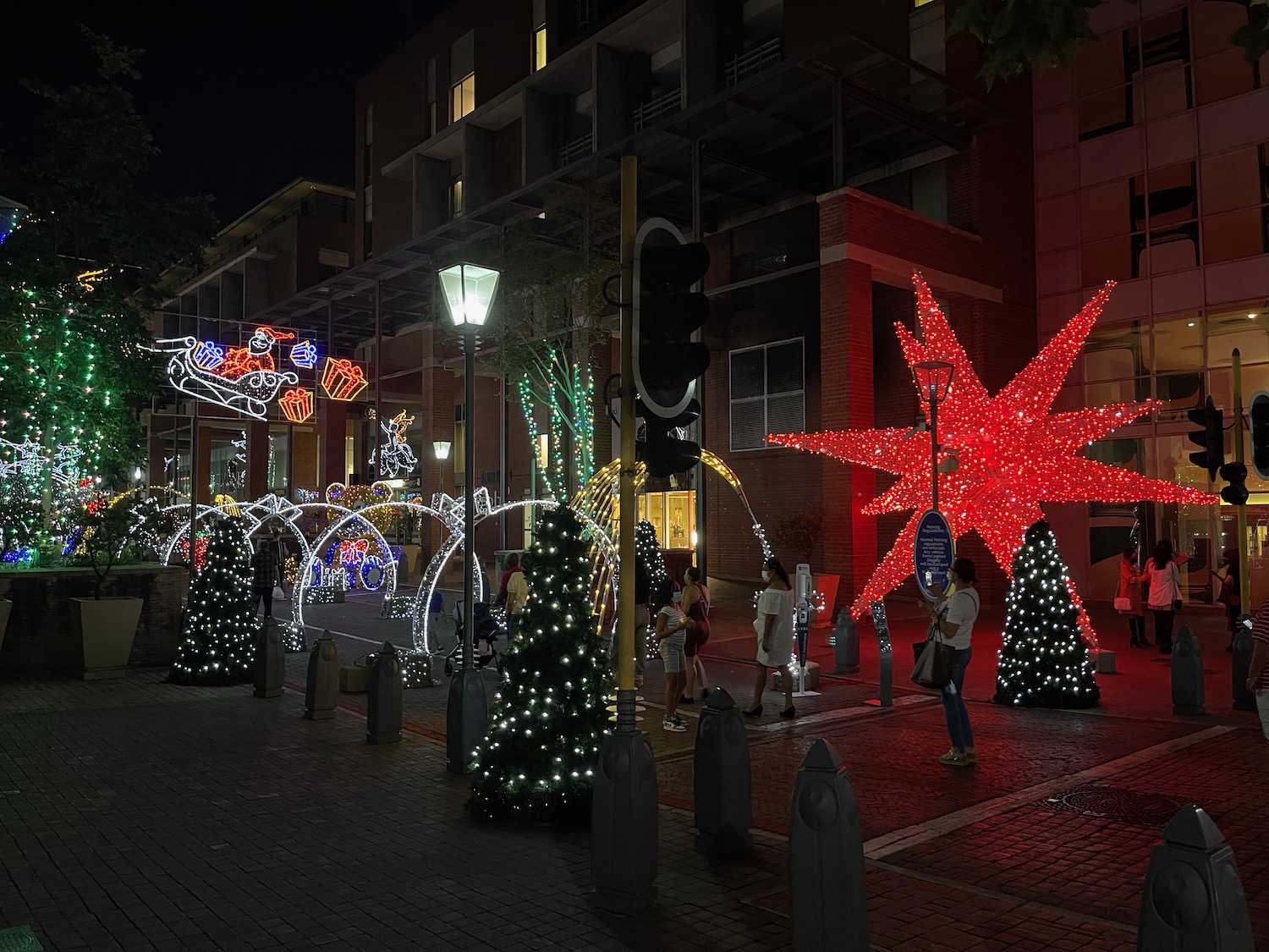 a group of people standing on a sidewalk with christmas lights