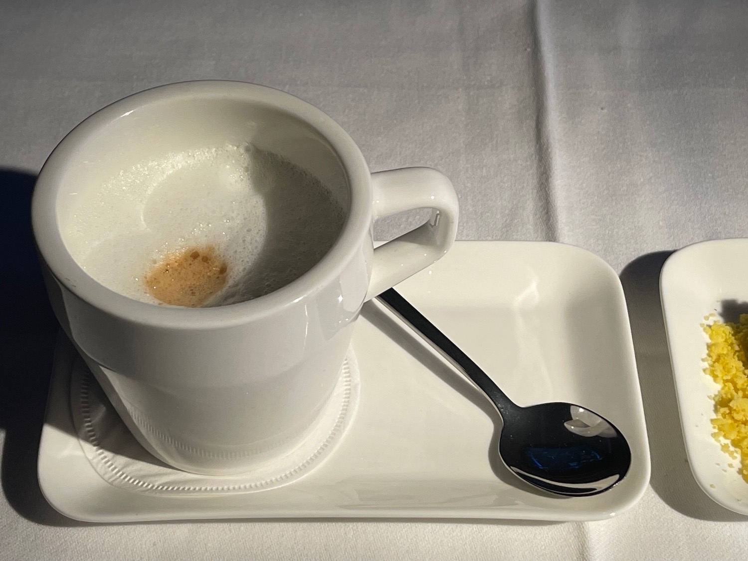 a white cup with a brown foam in it and a spoon on a white plate