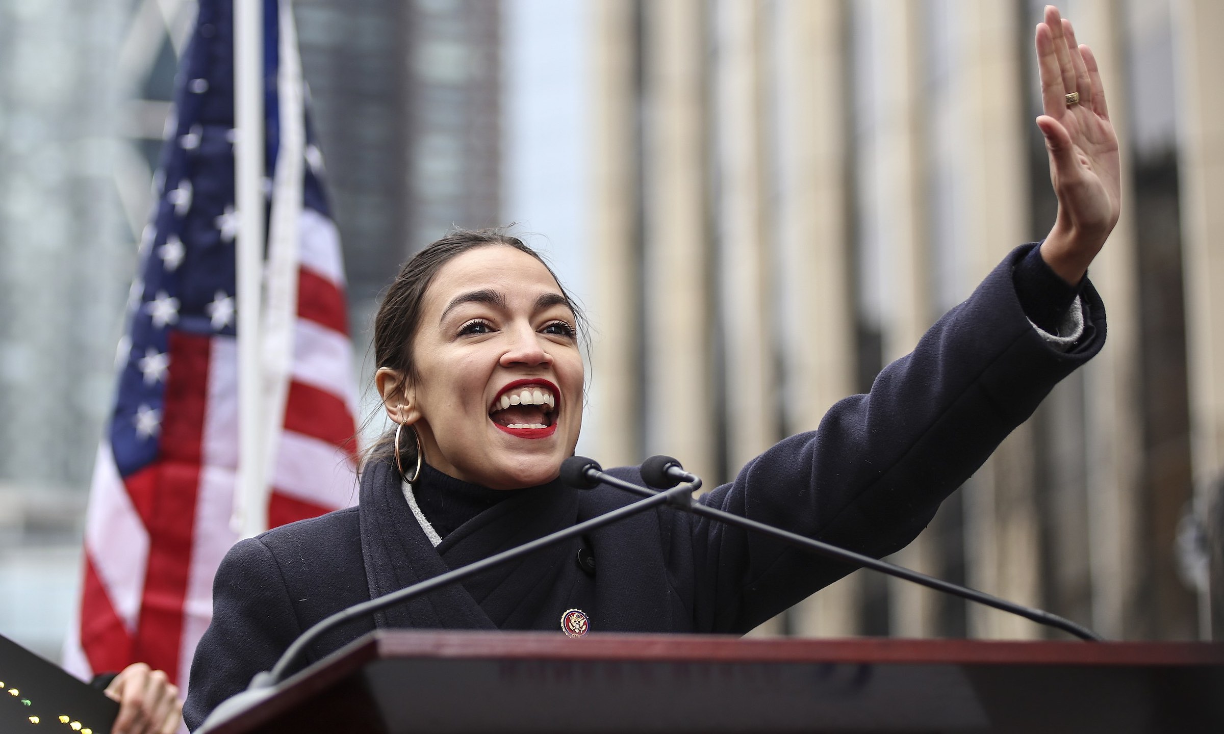 a woman standing at a podium with a microphone and a flag behind her