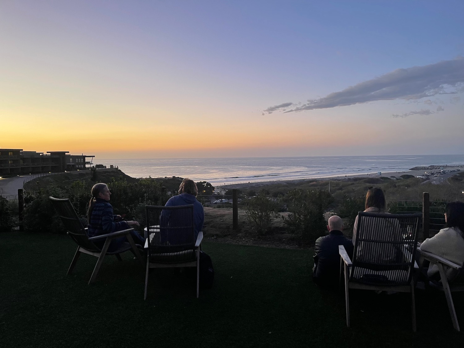 a group of people sitting in chairs on grass overlooking the ocean