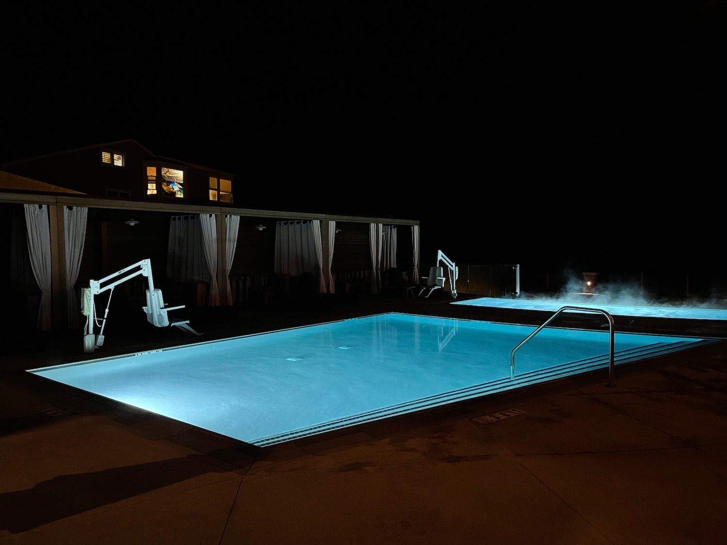 a pool with a hot tub and a building at night