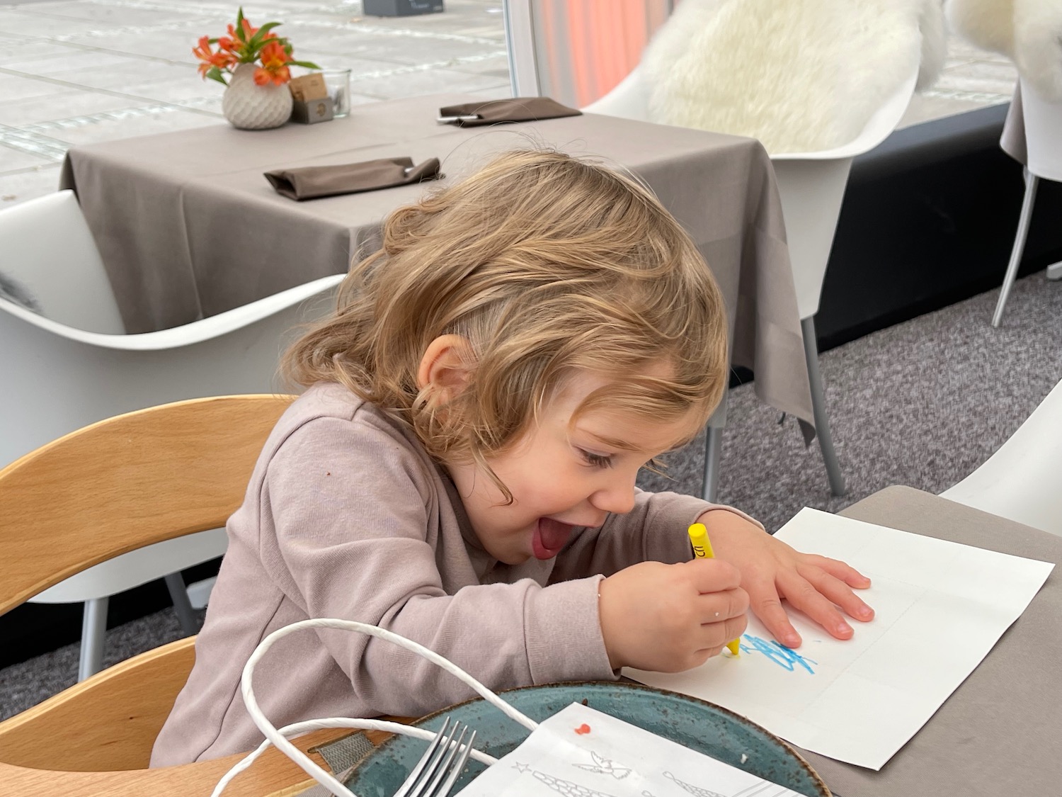 a child sitting at a table drawing with a yellow crayon