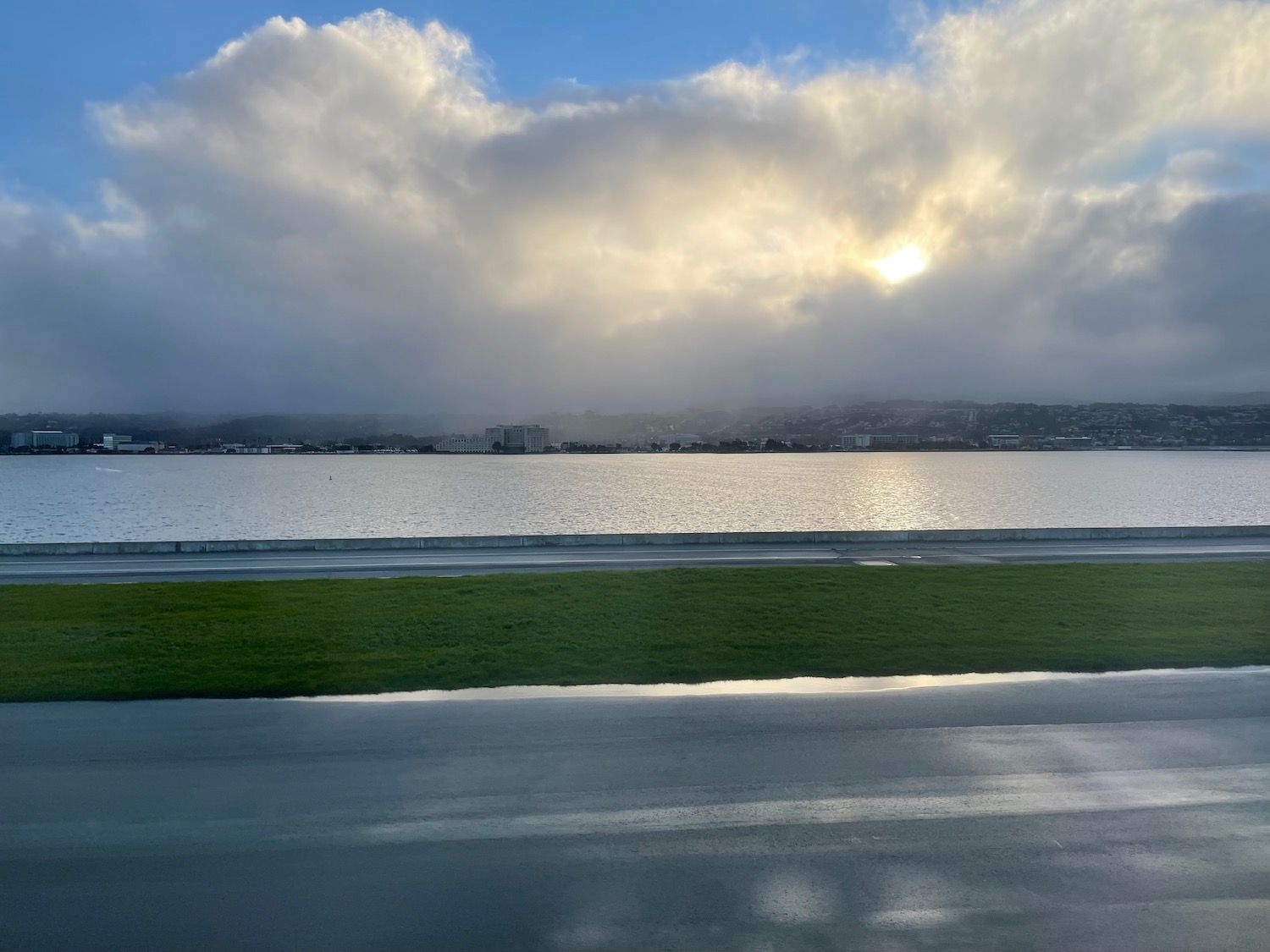 a road and water with clouds and a city in the background