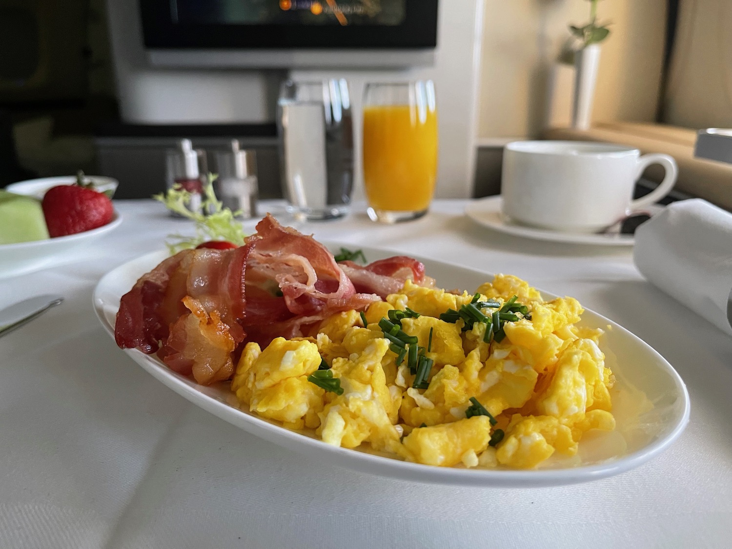 a plate of scrambled eggs bacon and greens on a table