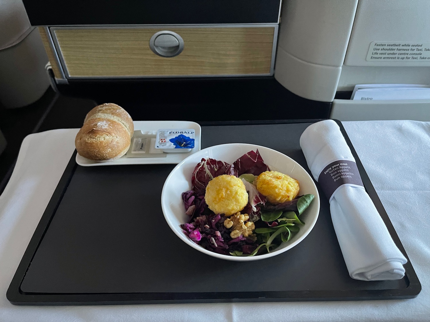 a bowl of salad and a roll on a tray