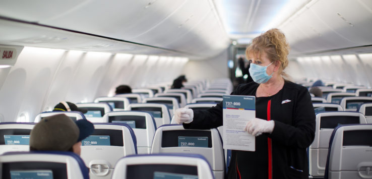 a woman wearing a mask and gloves holding a sign in an airplane