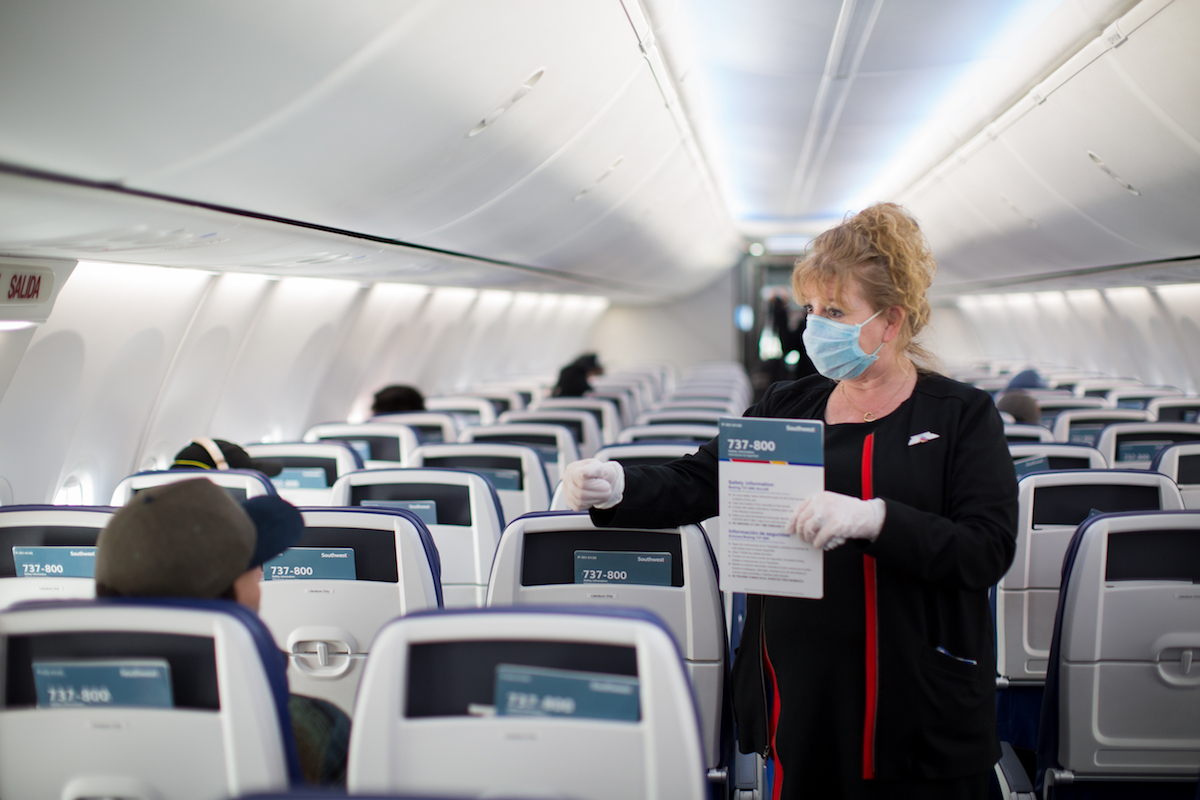 a woman wearing a mask and gloves holding a sign in an airplane