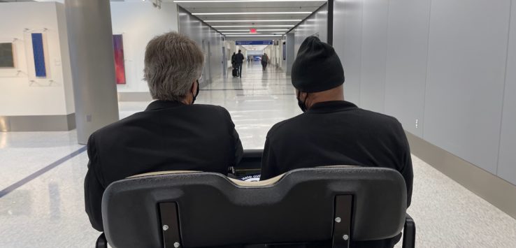 two men sitting in a wheelchair in a hallway