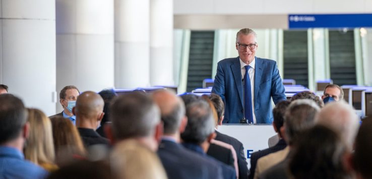 a man in a suit speaking at a podium with a crowd of people