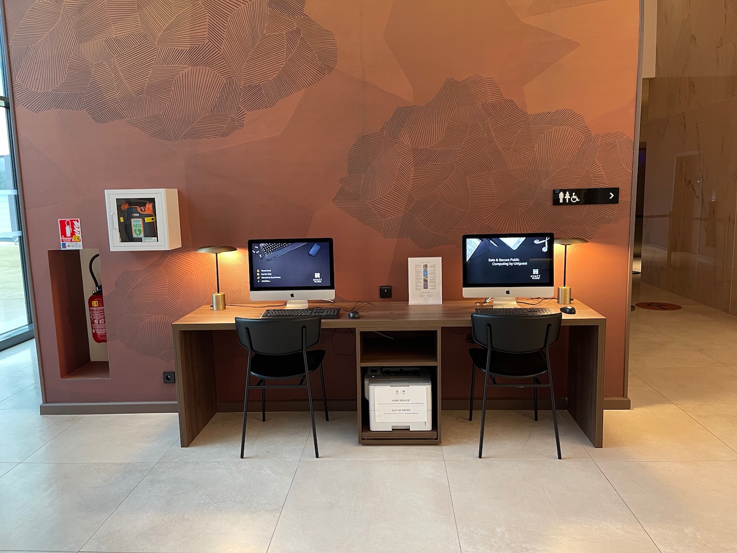 a desk with two computers and chairs in front of a wall