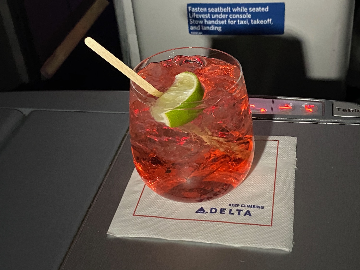 a glass of red liquid with a lime slice on a napkin